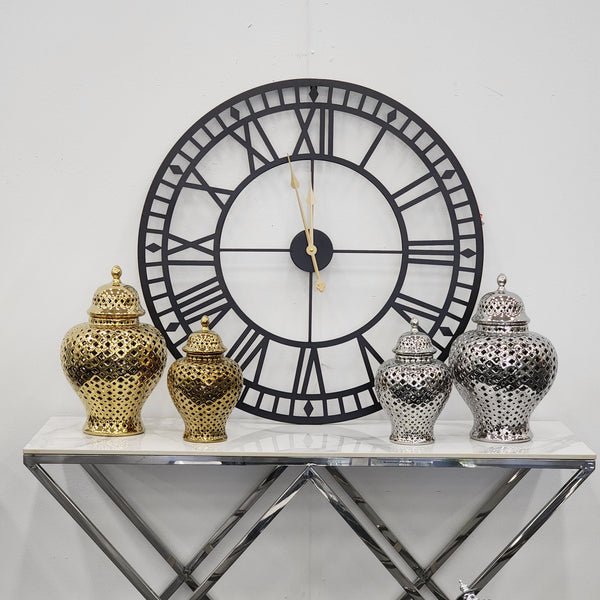 Styled display of Classic Hampton gold and silver ceramic urns placed on a mirrored console beneath a large black Roman numeral wall clock – a sophisticated home décor vignette.