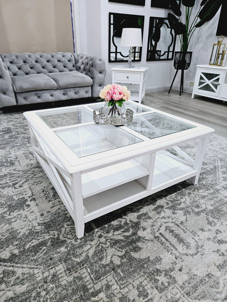 Hampton’s style square white coffee table with glass inlay styled with flowers on rug.
