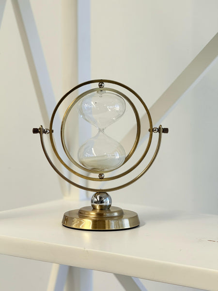 Stylish gold hourglass décor placed on a white shelf with modern interior background.