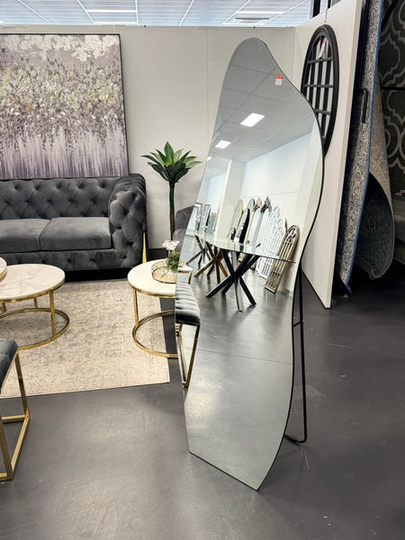 Irregular free standing mirror displayed in showroom with sofas, wall art and modern interior décor.