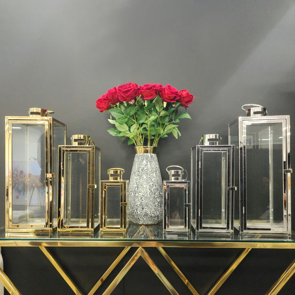Luxurious gold and silver lantern set styled with red roses on a modern glass console.