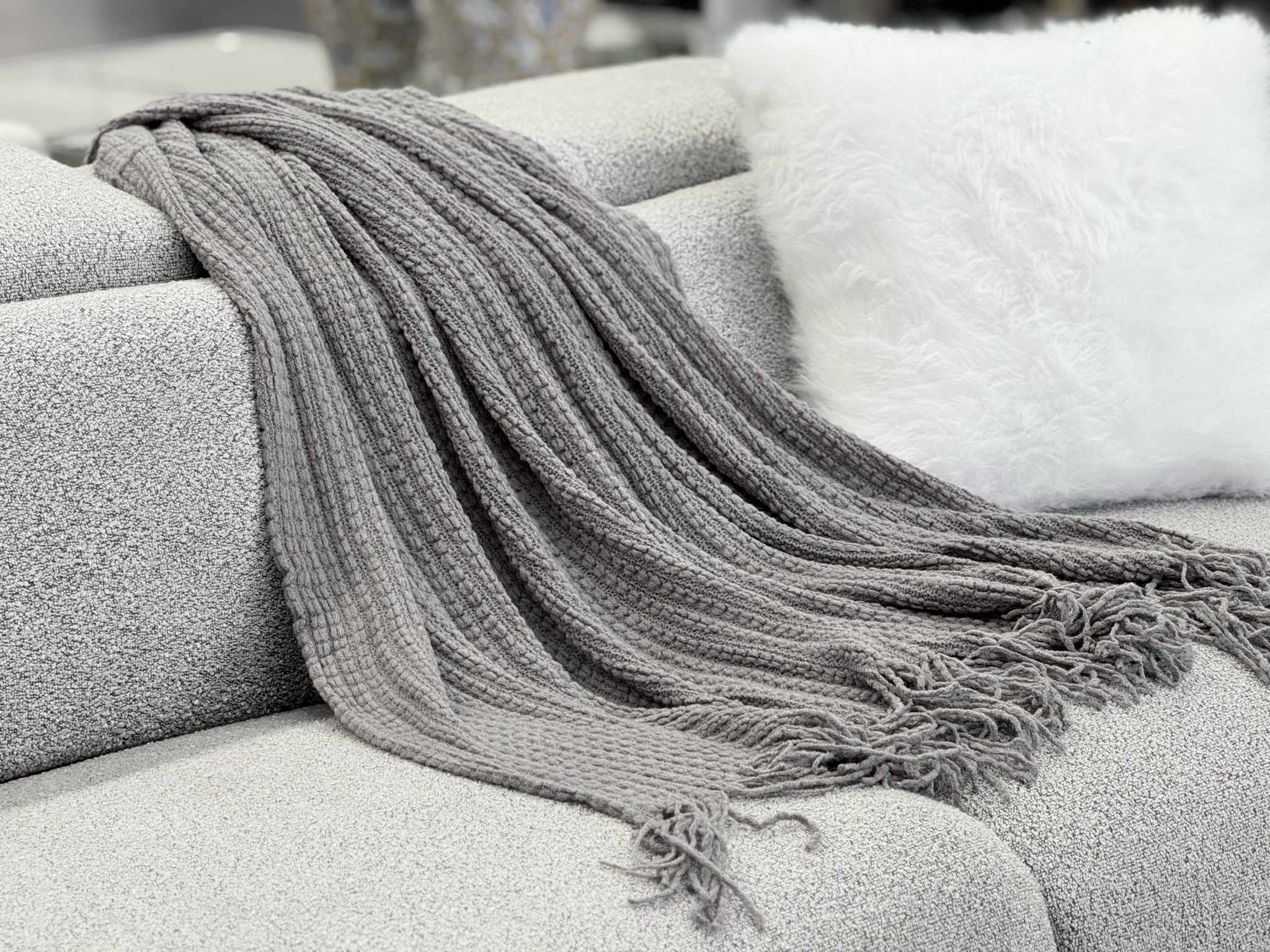 Cozy Levi Throw Rug Blanket in dark grey draped over a sofa, adding a touch of elegance with its fringe edges.