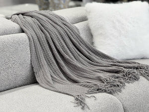  Cozy Levi Throw Rug Blanket in dark grey draped over a sofa, adding a touch of elegance with its fringe edges.