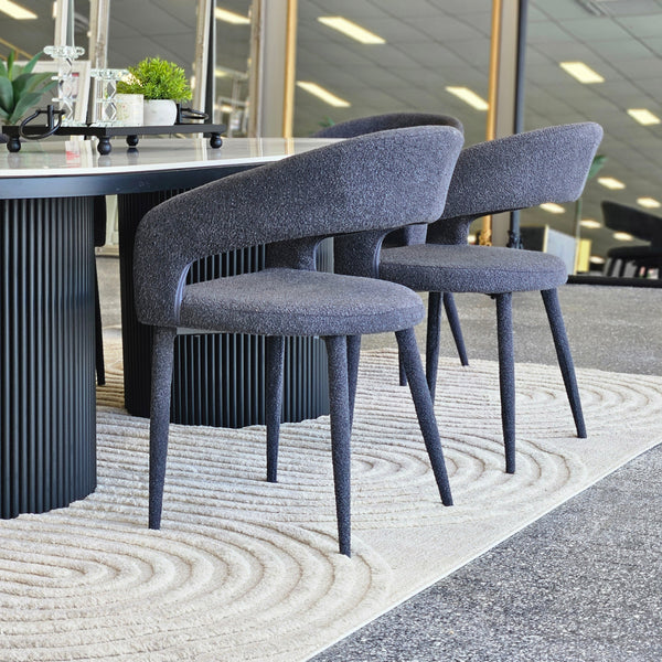 Pair of Marilyn boucle dining chairs in charcoal fabric styled around a black dining table in a modern setting.