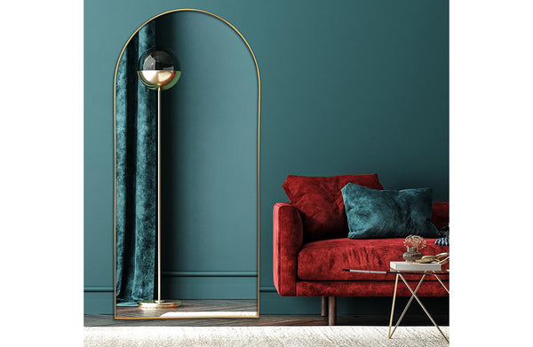 Tall gold metal arch mirror styled against deep green wall with red sofa
