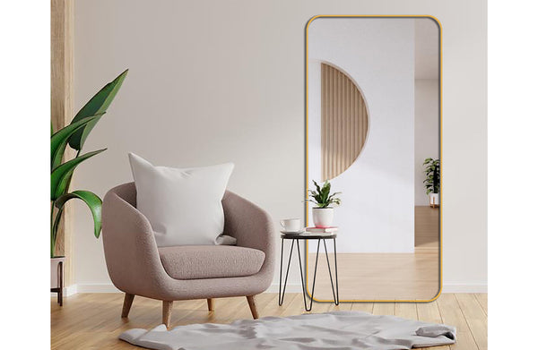 Tall gold metal rectangle mirror styled beside armchair and plant in modern interior