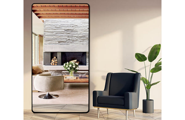 Extra-large black metal rectangle mirror styled in living room with fireplace and modern chair.