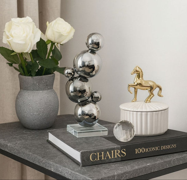A vase with white flowers, a modern ball sculpture, and a book titled '100 Iconic Designs' on a surface.