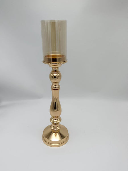 Tall gold pillar candle holder with a shiny base and amber-toned glass top, a striking piece for luxury interiors