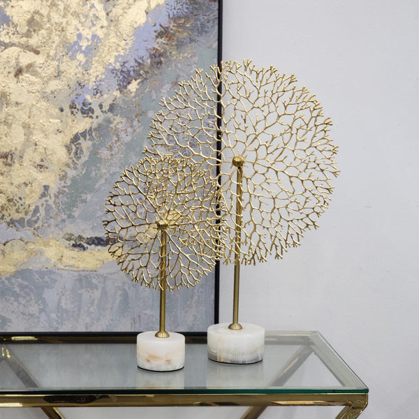 Stylish gold flower stem décor set on marble base, displayed on a glass table with elegant wall art in the background.